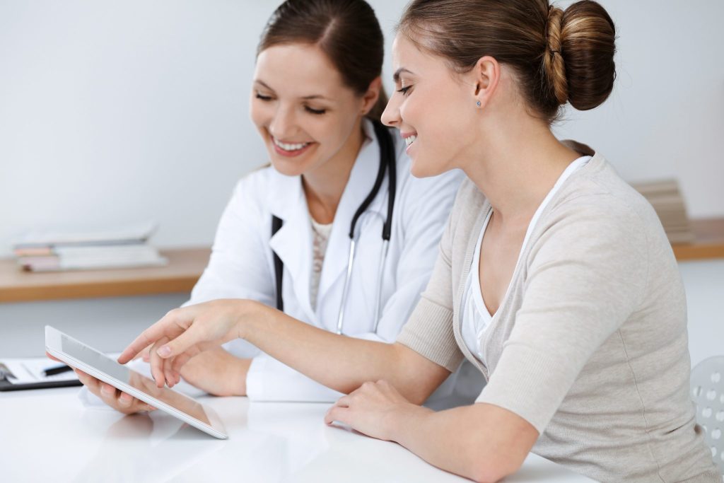 A female doctor and her patient, a young woman, sitting at a desk and discussing test results.