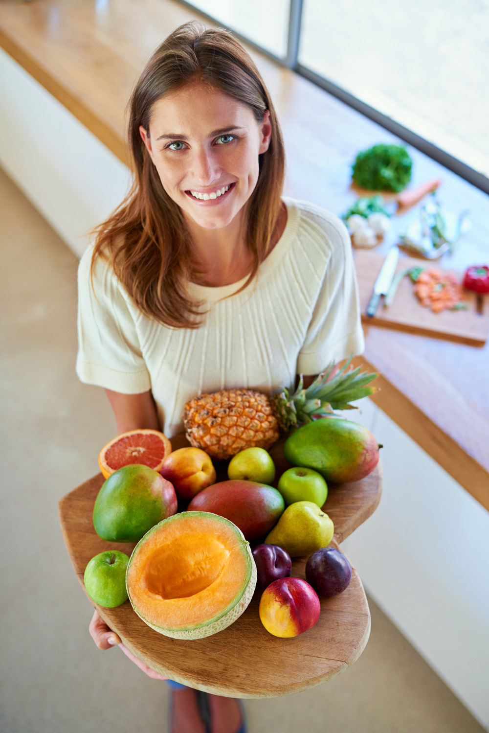 A woman in her thirties holding a basket of fresh fruit and smiling